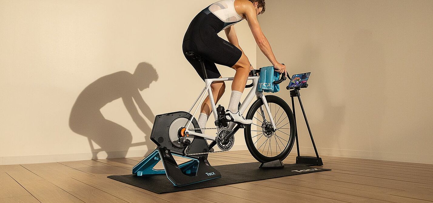Ein Radfahrer sitzt in einem Raum auf einem auf einem Smarttrainer montierten Rennrad. 